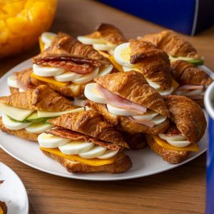 Paris Baguette croissant breakfast sandwiches filled with ham, egg, cheese, and bacon, served on a catering platter.