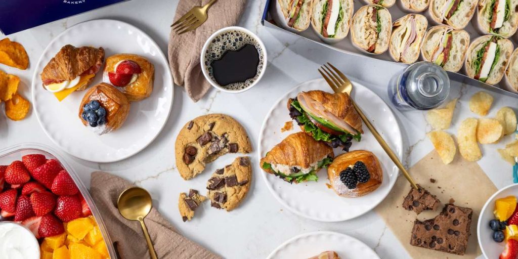 Catering spread with freshly baked croissant sandwiches, assorted pastries, wrap platters, fresh fruit, coffee, cookies, and brownies from Paris Baguette Catering.