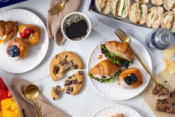 Catering spread with freshly baked croissant sandwiches, assorted pastries, wrap platters, fresh fruit, coffee, cookies, and brownies from Paris Baguette Catering.